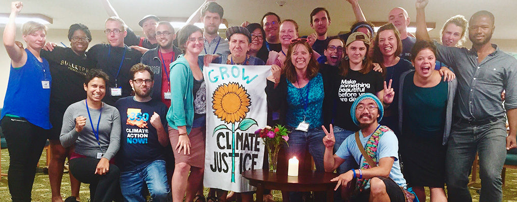 A multiracial group of two dozen young adults cheers and holds a banner that says "Grow Climate Justice"